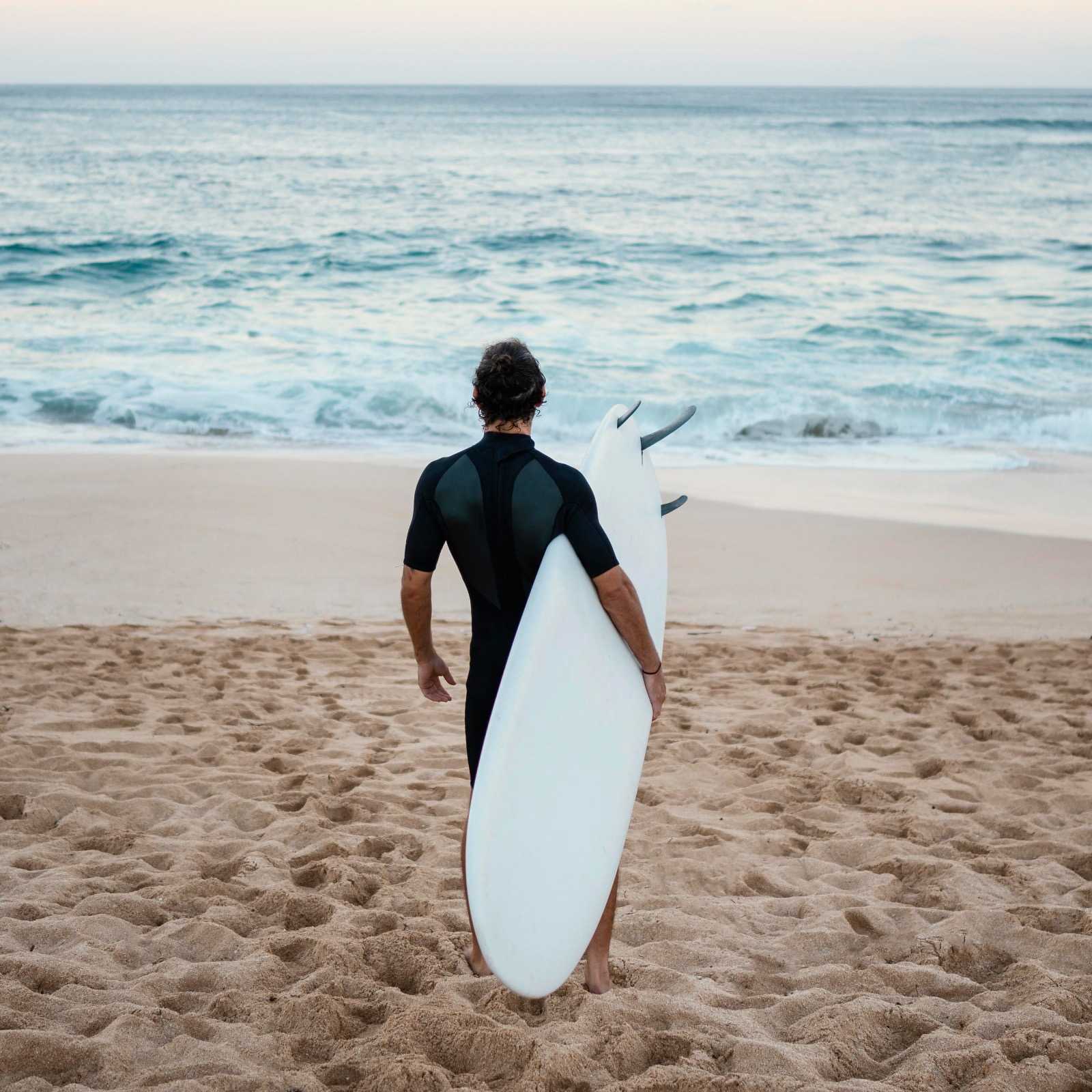 A participant walking toward the ocean with a surfboard