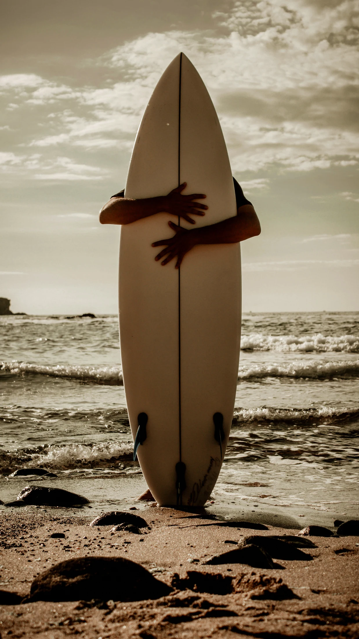 A person holds their surfboard facing the ocean